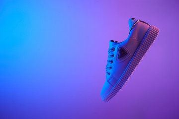 Trendy white teenage sneaker flying in trendy neon light. Levitation Shoe in red, blue light. Creative minimalism.