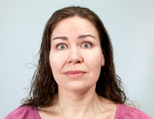Fototapeta premium Wide-open eyes and a tense neck with fright in an adult woman, portrait on grey background, emotions series.