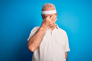 Middle age hoary sportsman doing sport wearing sportswear over isolated blue background tired rubbing nose and eyes feeling fatigue and headache. Stress and frustration concept.