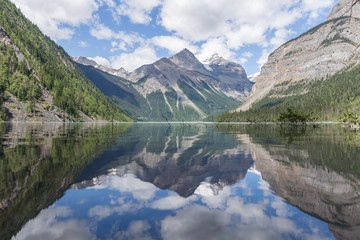 mountains, blue sky and clouds reflect in the calm water of a lake