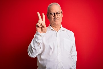Fototapeta premium Middle age handsome hoary man wearing casual shirt and glasses over red background smiling looking to the camera showing fingers doing victory sign. Number two.