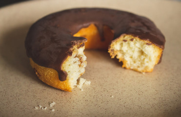 Bitten chocolate donut filtered. Homemade donut toned image. Fresh bakery. Sweet round cake glazed with chocolate. Bitten chocolate doughnut on plate. Tasty pastry concept. Sweet breakfast concept. 