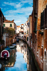 Fototapeta na wymiar Close up. Street view of a canal with wooden boats and stone bridges between old brick buildings with tiled roofs, shutters and chimneys in the center of Venice, Veneto, Italy. European architecture.
