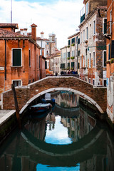 Venice, Veneto, Italy - February 29, 2020 - View of a canal with wooden boats, stone bridges between old brick buildings with tiled roofs, shutters, chimneys in the city center. European architecture.