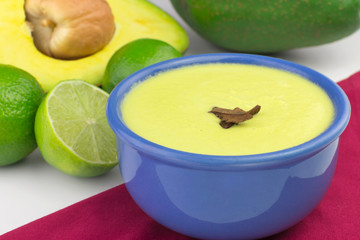 Avocado cream in a blue bowl with avocados and lemons in the background