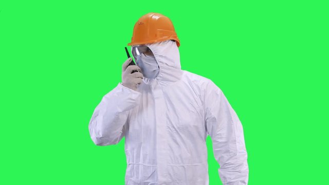 A man in a helmet and a protective suit in his hands holds a walkie-talkie goes forward.Green screen background.