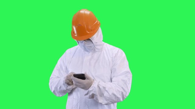 A man in a helmet and protective suit is surfing the phone.Green screen background.