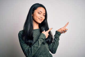 Young beautiful chinese woman wearing casual t-shirt over isolated white background smiling and looking at the camera pointing with two hands and fingers to the side.