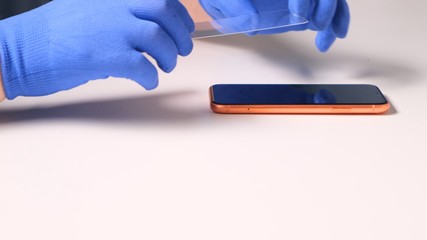 male hands in blue gloves replaces a broken tempered glass screen protector for a smartphone. A man prepares a smartphone to replace glass. Smartphone repair concept. copy space