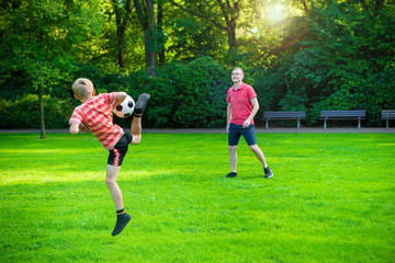 Obraz premium Happy young father play with his little son football in sunny park