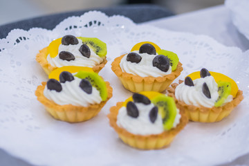 Assortment of delicious fresh shortcrust tart cakes with cream and fruits for sale on white plate at cuisine of restaurant, cafe. Dessert, culinary, sweet food and confectionery concept