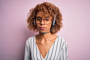 African american curly call center agent woman working using headset over pink background skeptic and nervous, frowning upset because of problem. Negative person.