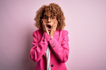 Young african american businesswoman wearing glasses standing over pink background afraid and shocked, surprise and amazed expression with hands on face