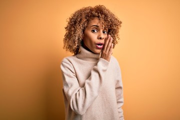 Fototapeta na wymiar Young beautiful african american woman wearing turtleneck sweater over yellow background hand on mouth telling secret rumor, whispering malicious talk conversation