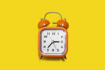 Vintage style orange metal alarm clock with bells standing on the yellow background isolated. back to school concept