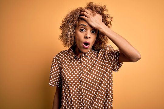 Young beautiful african american woman wearing casual shirt standing over yellow background surprised with hand on head for mistake, remember error. Forgot, bad memory concept.