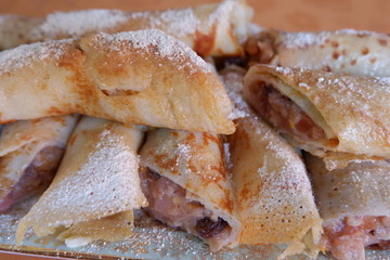 Close view of the pile of pancake rolls with apple mousse and powdered sugar on top