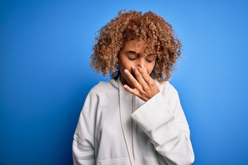 Fototapeta na wymiar Beautiful african american sporty woman wearing casual sweatshirt over blue background smelling something stinky and disgusting, intolerable smell, holding breath with fingers on nose. Bad smell