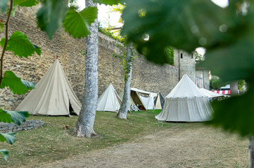 Nachstellung einer Mittelalterszene vor historischer Kulisse einer alten Stadtmauer, Dorf mit Zelten verschiedener Bauart mit Details der Stoffe und Heringe, Seile und Verspannung, Blick in Zelte