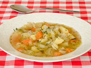Italian cabbage soup in a white plate on a plaid tablecloth.