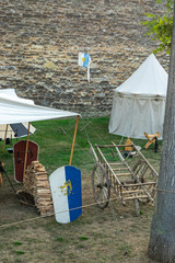 Mittelalterszene vor historischer Kulisse einer alten Stadtmauer, Dorf mit Zelten verschiedener Bauart, Blick in Zelte, Dorfplatz mit Utensilien und Gefäßen, Möbeln, Holzlager und Transportkarre