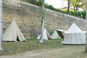 Nachstellung einer Mittelalterszene vor historischer Kulisse einer alten Stadtmauer, Dorf mit Zelten verschiedener Bauart mit Details der Stoffe und Heringe, Seile und Verspannung, Blick in Zelte