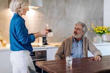 Mature couple celebrating birthday with cake in kitchen at home