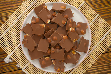 Delicious milk chocolate with hazelnuts on wooden background