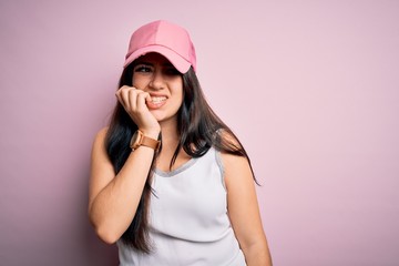 Young brunette woman wearing casual sport cap over pink background looking stressed and nervous with hands on mouth biting nails. Anxiety problem.