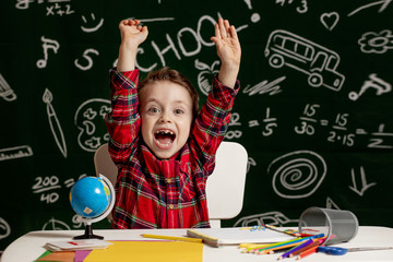 Emotional school boy sitting on the desk with many school supplies. First day of school. Kid boy from primary school. Back to school. Child from elementary school.