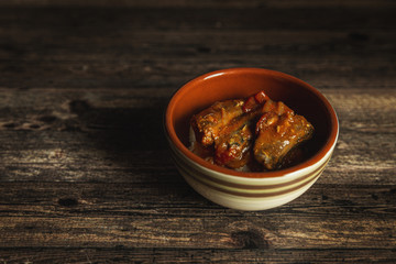 Canned sardines cooked in a tomato sauce served in a rustic bowl on wooden table.