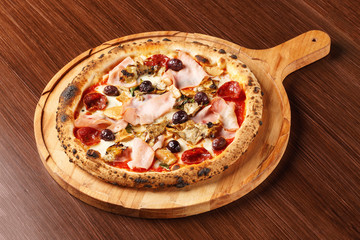 Pontremolina. Hot Italian pizza with Piennolo tomatoes, turkey ham, artichokes, oregano and salami. Original recipe. Pizza on wooden background