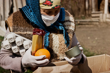An elderly woman in a mask examines products in a box delivered by a courier during quarantine....