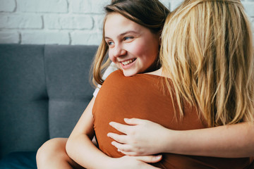 people and family concept - happy smiling girl with mother hugging on sofa at home.Happy mother's day! Mom and her daughter child girl are hug. Family holiday and togetherness - 341072304