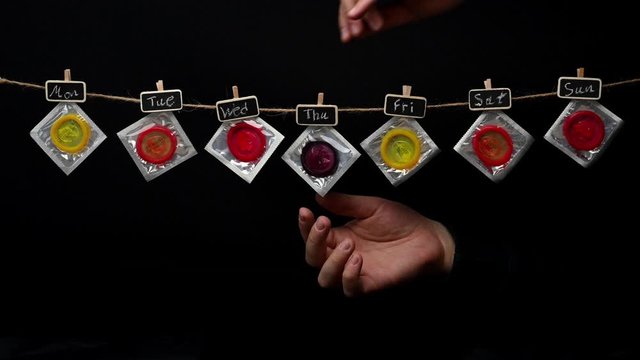 Condoms hanging on string with days of the week and hand selecting one