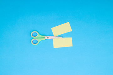 Green scissors and cut colored paper on blue background 