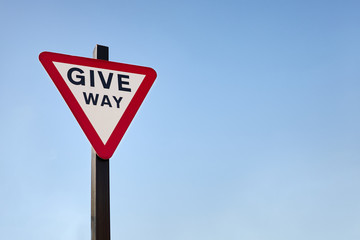 Isolated British give way traffic sign against blue sky background. Space for copy text. Red upside down triangle.