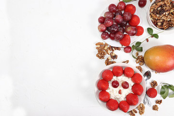 Useful breakfast, food for children, Strawberry yogurt, granola, cottage cheese, honey, mango, strawberries and grapes on a light table. The concept of healthy and natural food. selective focus,