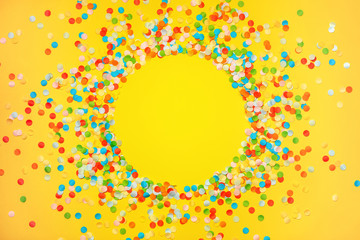 Naklejka na ściany i meble Yellow background with vivid confetti. Colorful abstract backdrop with round frame and space for your text. Festive composition for celebration. View from above. Flat lay