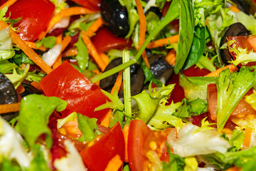 Vegetable salad sliced tomatoes, carrots, beets, lettuce, arugula and olives. Close-up background image.
