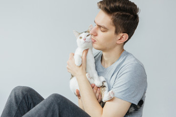 Young man with cat on light grey background. Favorite pet. Man holding cat
