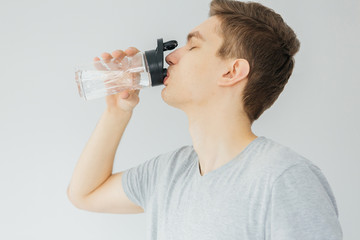 Young man in grey shirt drinking water during the sport. Sport at home. Man on grey background