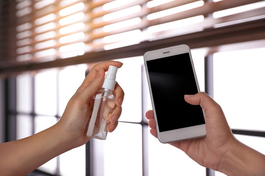 Woman sanitizing smartphone with antiseptic spray indoors, closeup. Be safety during coronavirus outbreak - Powered by Adobe