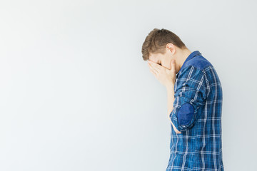 A young man covers his face with his hands. Problems and stress. Sad man on a light gray background