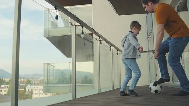 Stay at home. Father and son play in football on terrace of their apartment. Family spend free time. Weekend Holidays, Isolated concept. Social distancing. 4K video.