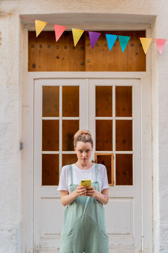 Portrait of young woman with smartphone standing in front of wooden door