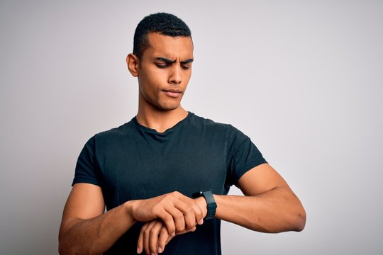 Young handsome african american man wearing casual t-shirt standing over white background Checking the time on wrist watch, relaxed and confident