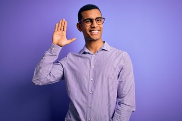 Handsome african american man wearing striped shirt and glasses over purple background Waiving saying hello happy and smiling, friendly welcome gesture