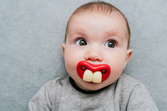 Portrait of baby girl with big teeth pacifier lying on grey blanket