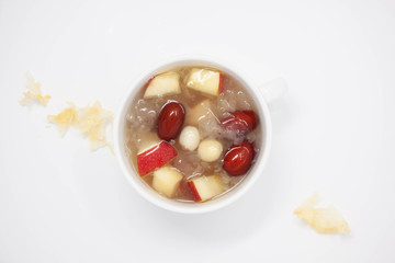 Top view of a bowl of white fungus soup with red apple, lotus seeds and red dates.